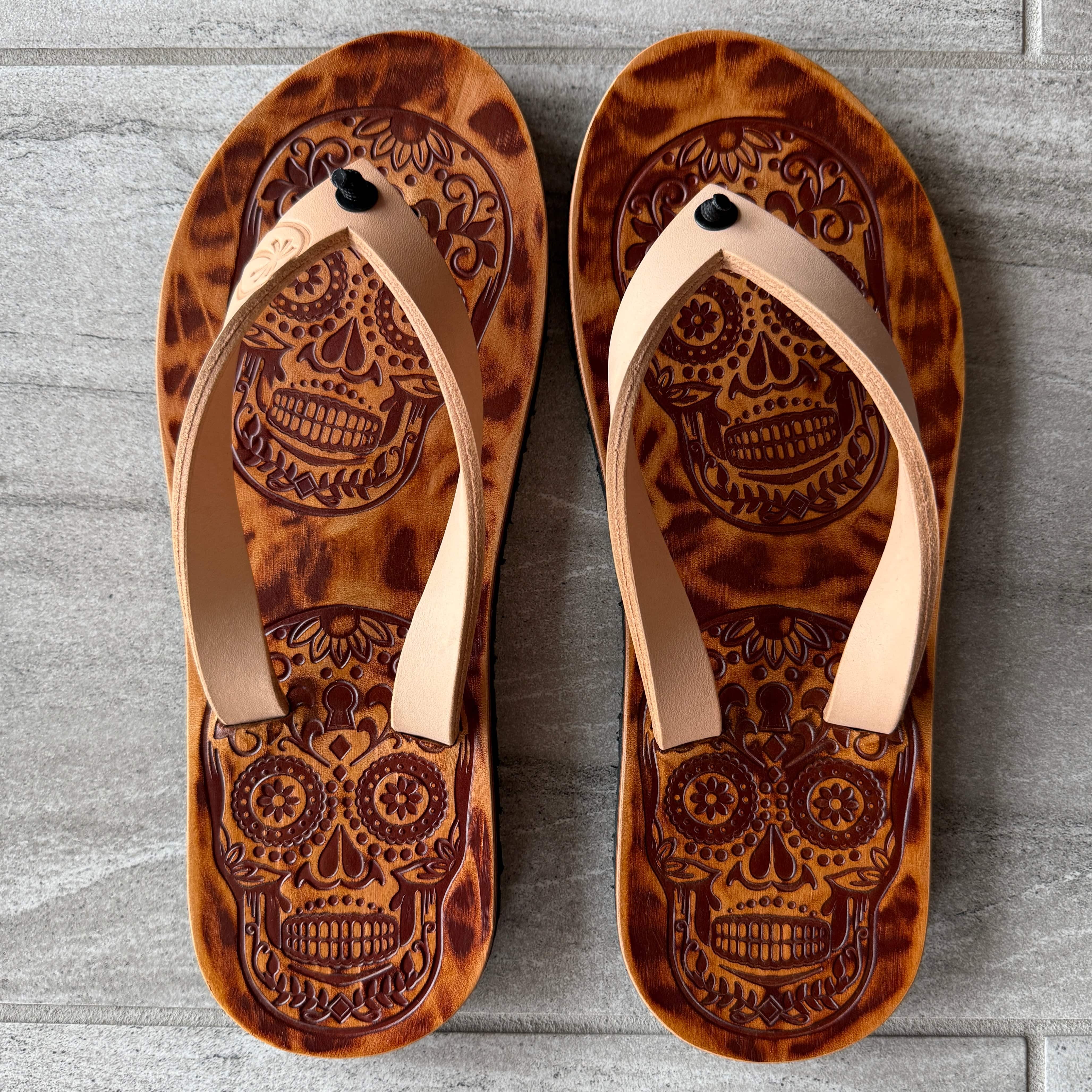 Toehold skull flip-flops featuring black straps and a skull graphic design on the footbed, casual summer footwear.