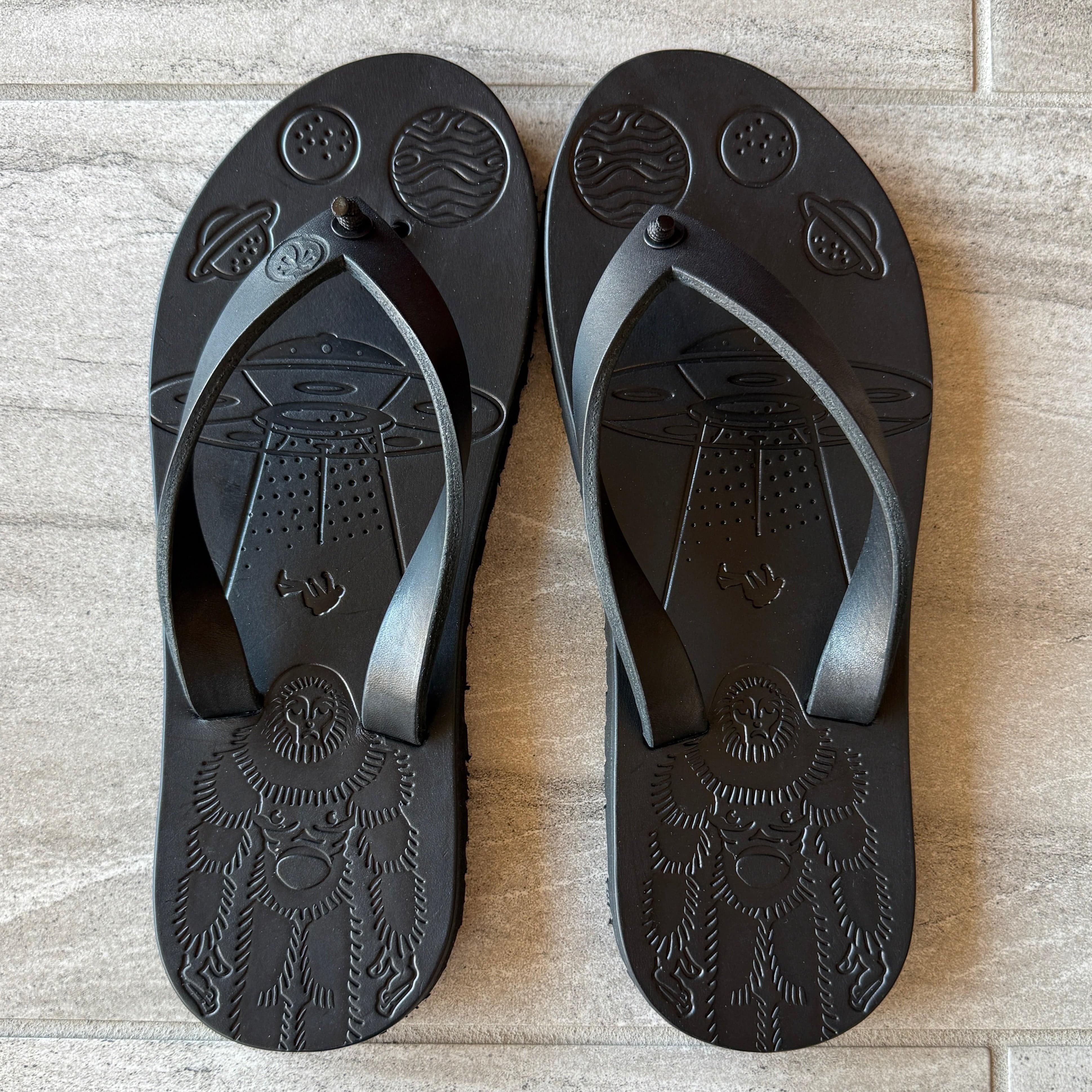 Black "Bigfoot" flip-flops by Toehold with thick straps and large sole, shown from a front angle on a plain background.