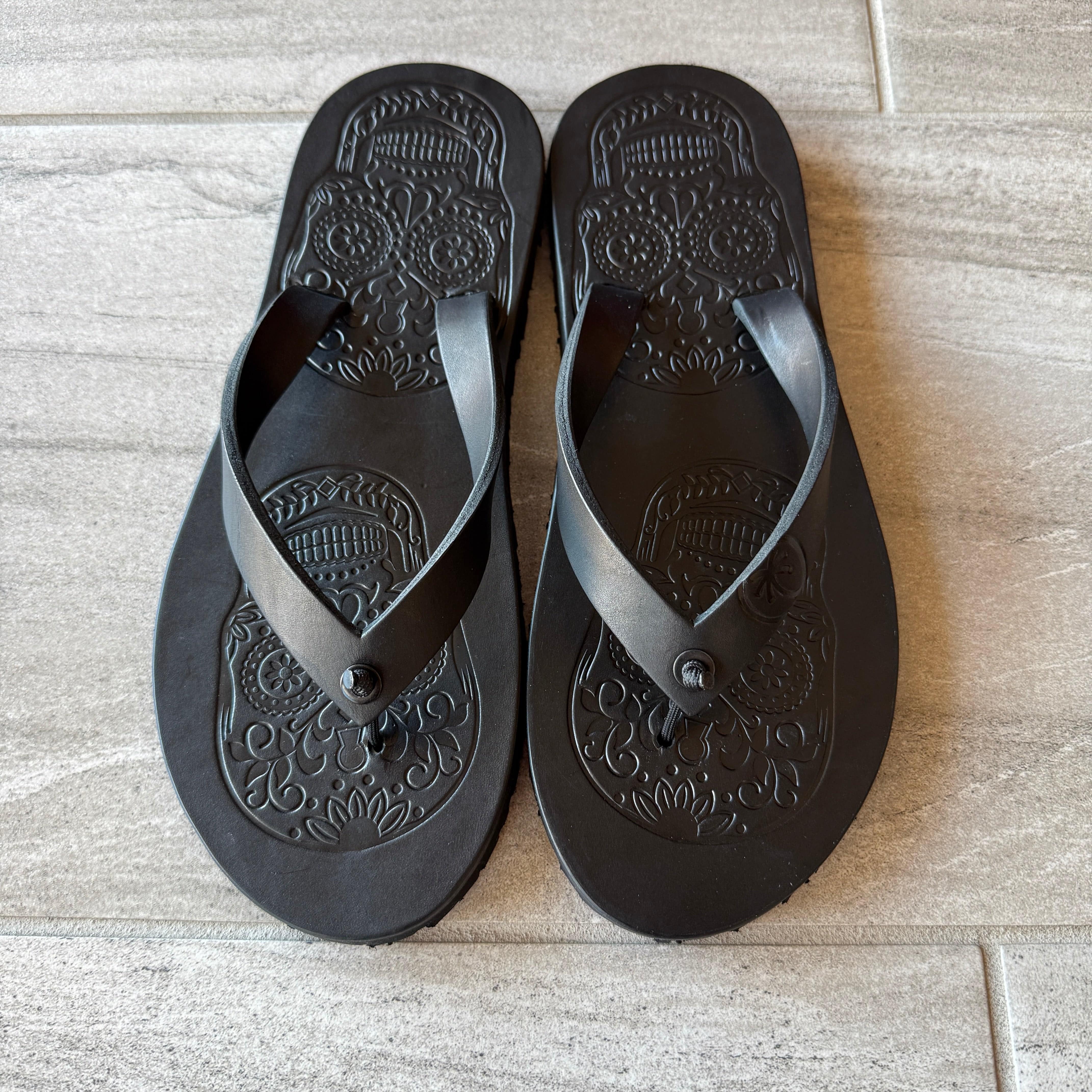 Black Skull Flip-Flops by Toehold featuring a skull design on the straps, casual footwear for warm weather.