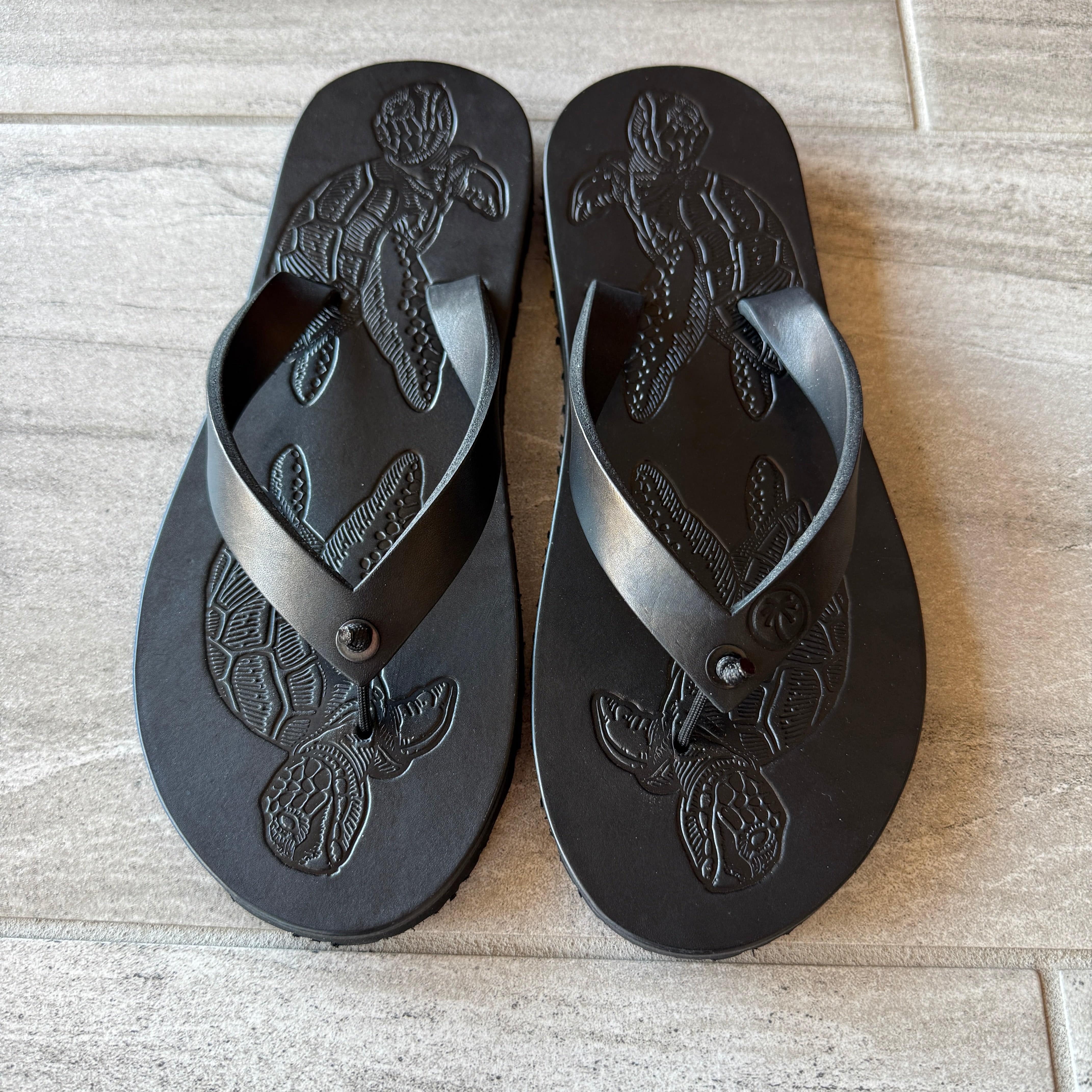 Toehold black sea turtle flip-flops with a detailed sea turtle design on the straps and soles.