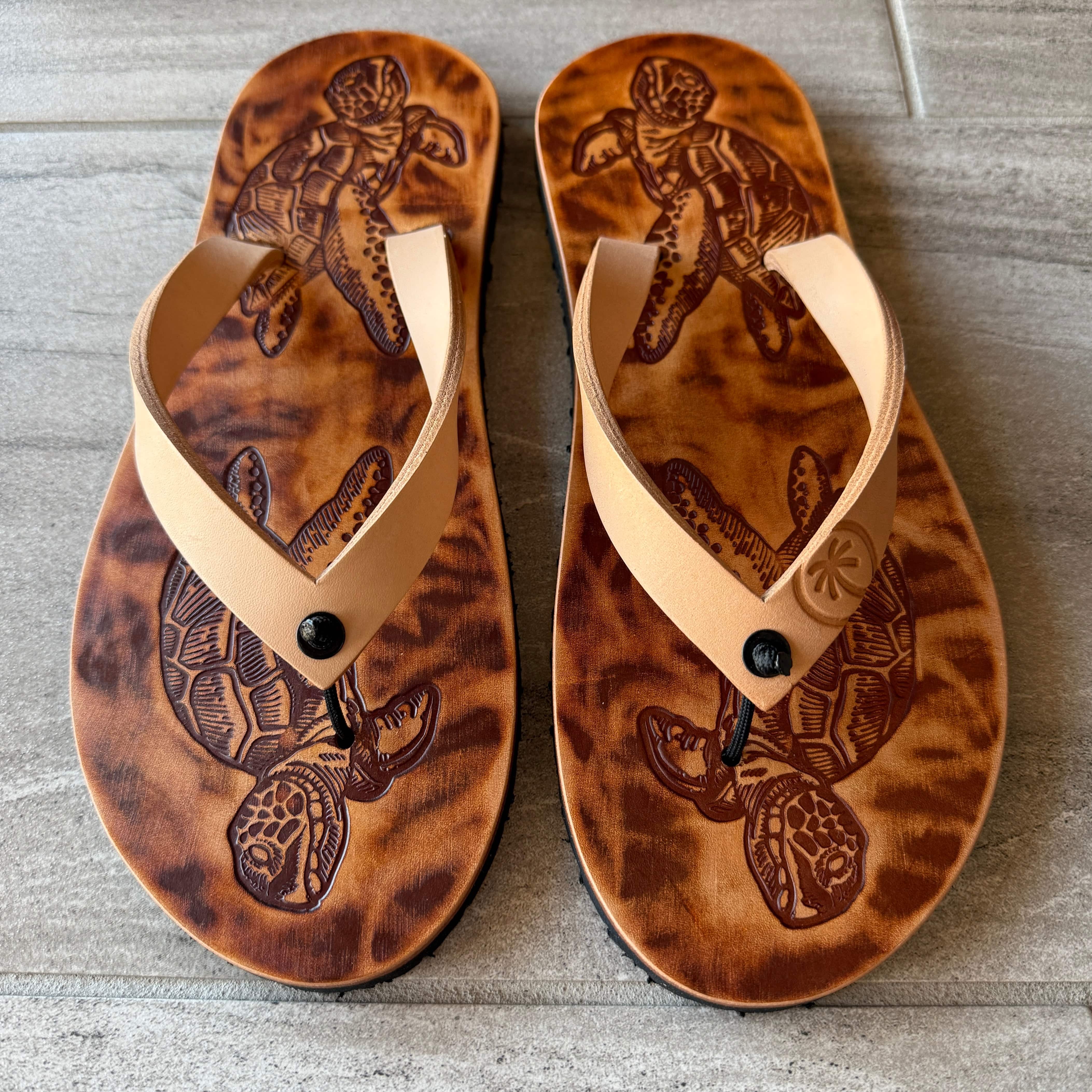 Toehold sea turtle flip-flops with green and brown straps featuring a sea turtle design on the footbed.