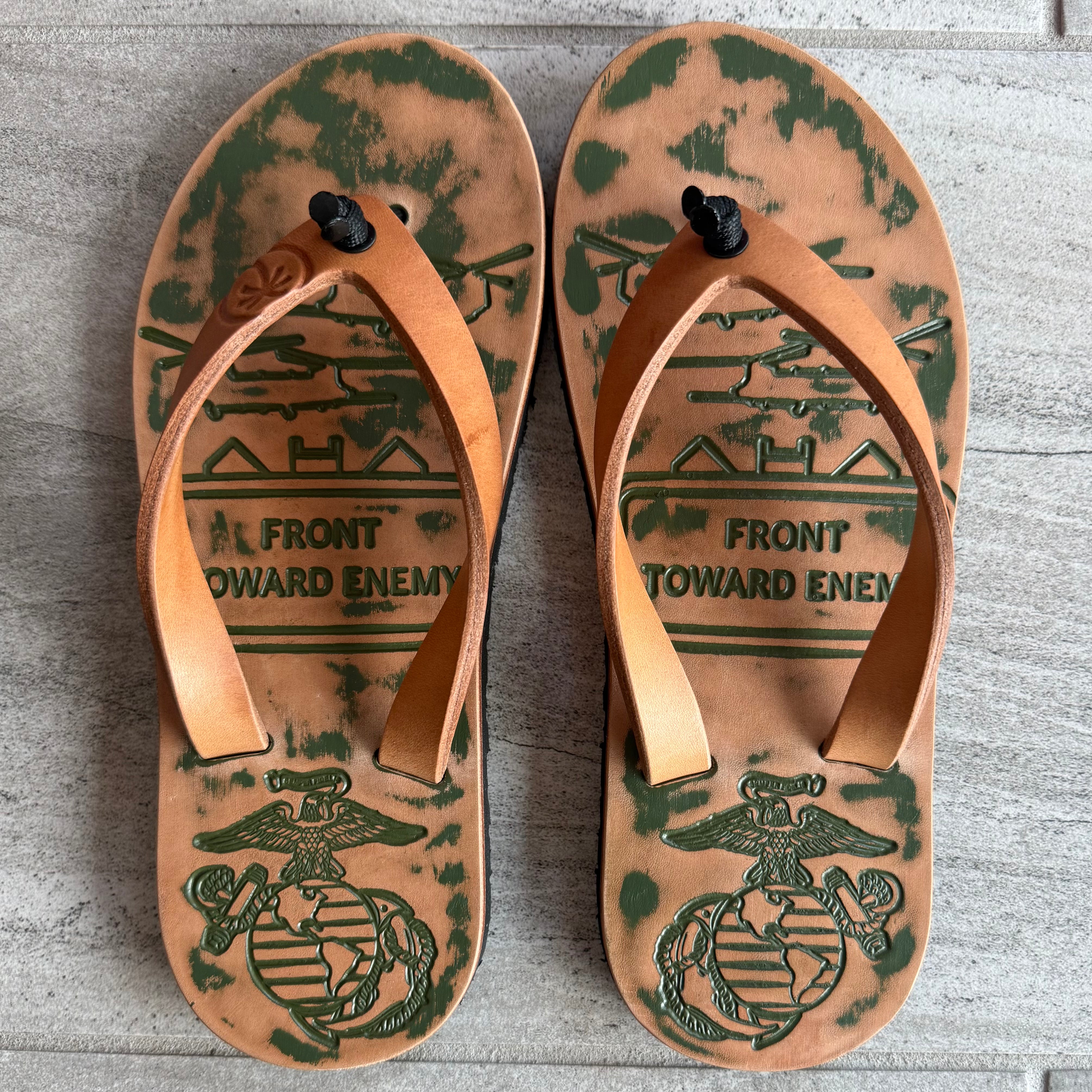 Toehold USMC flip-flops featuring the Marine Corps logo and camouflage straps, displayed on a plain background.