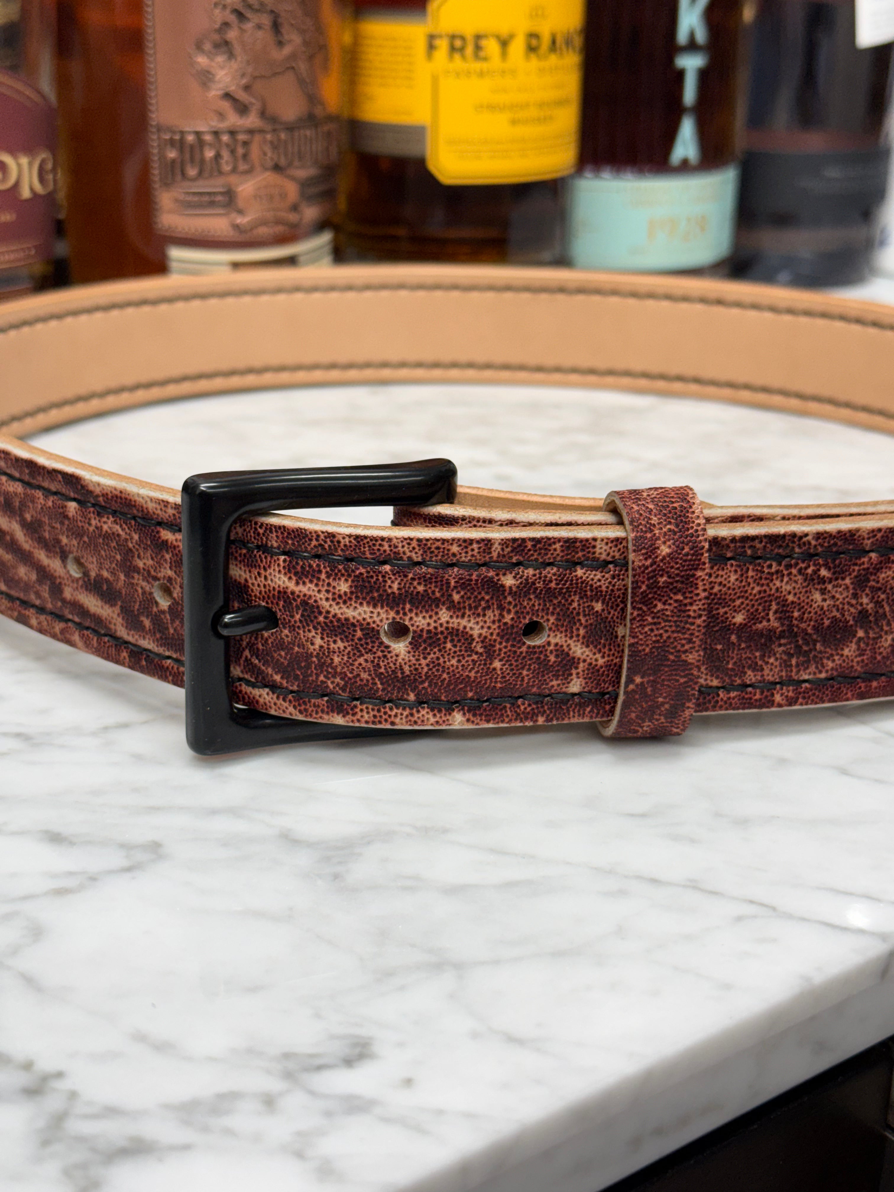Toehold Man Killing Elephant belts displayed in a close-up image showing detailed leather craftsmanship.