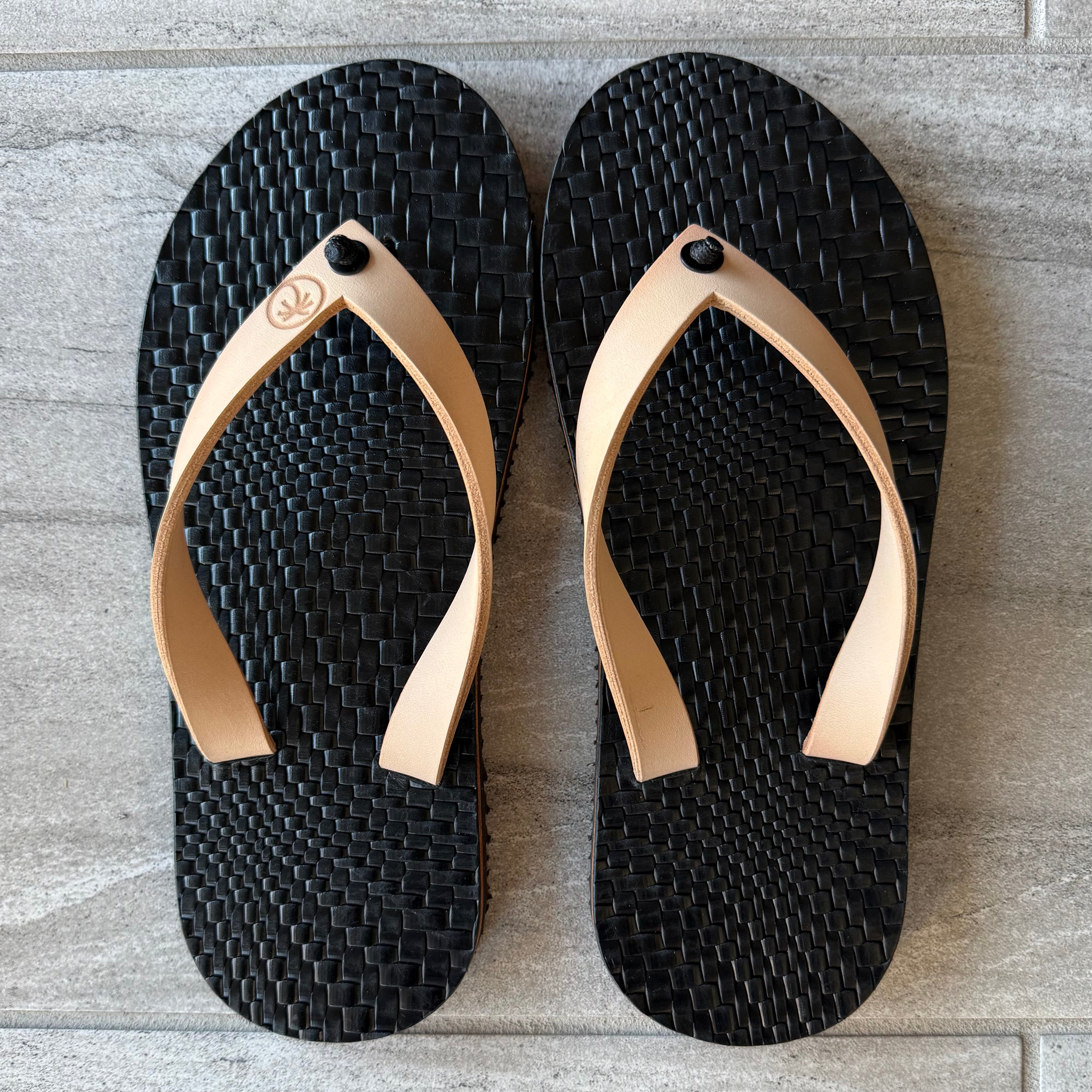 Black grenade-themed flip-flops by Toehold with textured sole and adjustable straps, designed for casual wear.