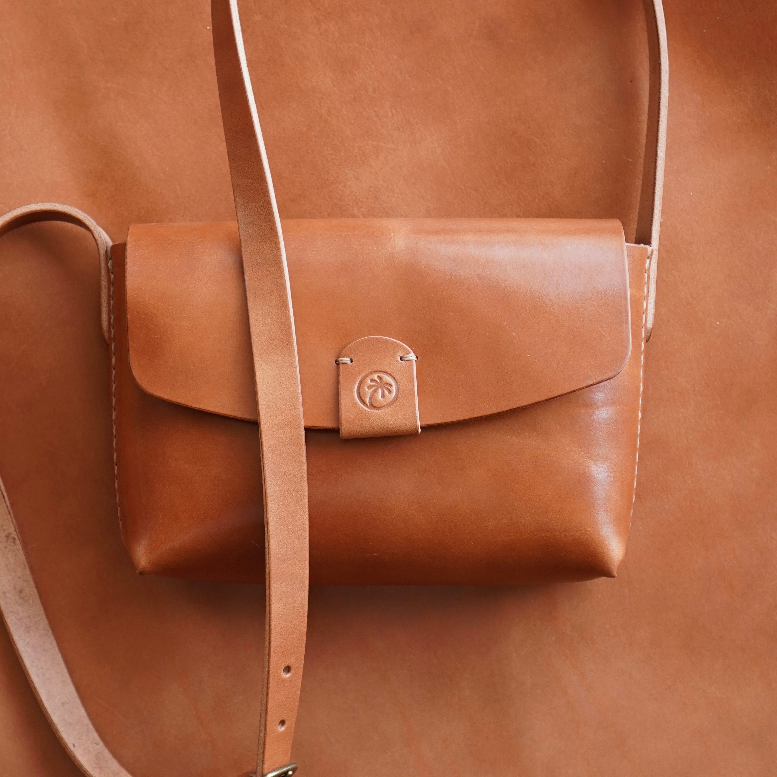 Toehold® Bag featuring a sleek design with a top handle and adjustable strap, shown in black leather material.