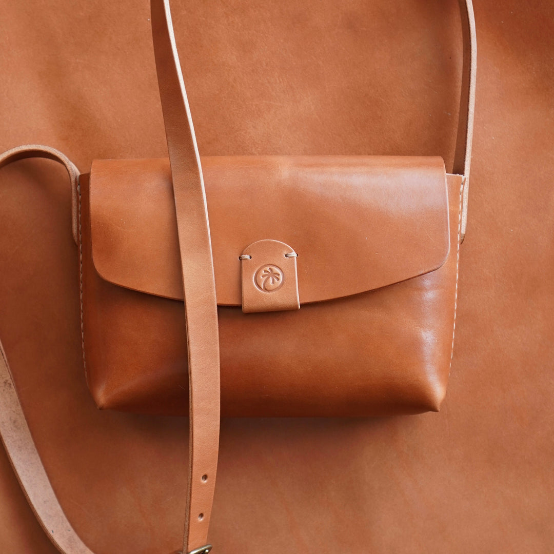 Toehold® Bag featuring a sleek design with a top handle and adjustable strap, shown in black leather material.