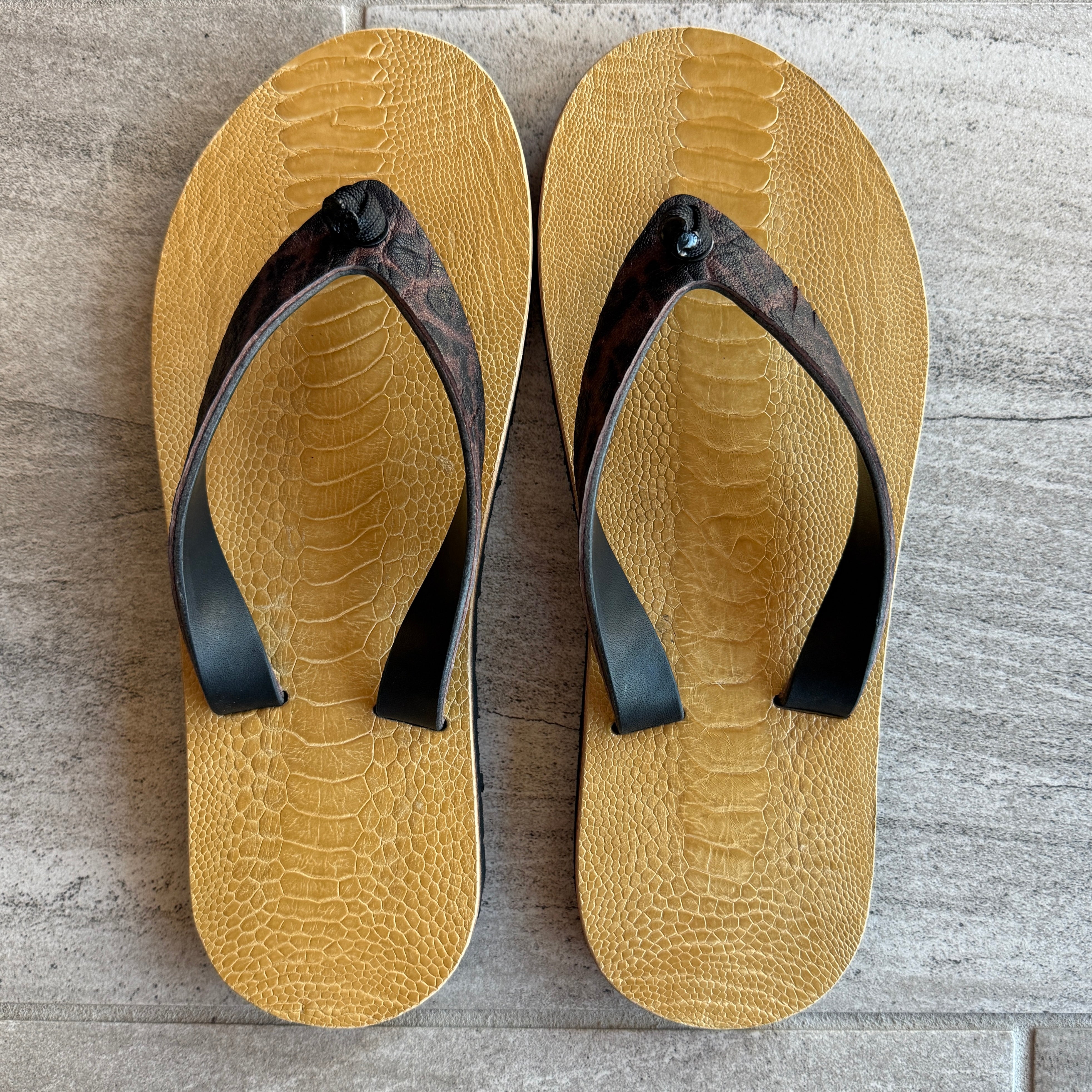 Men's Toehold flip-flops with 9 ostrich and elephant strap design, featuring black straps and comfortable sole for casual wear.